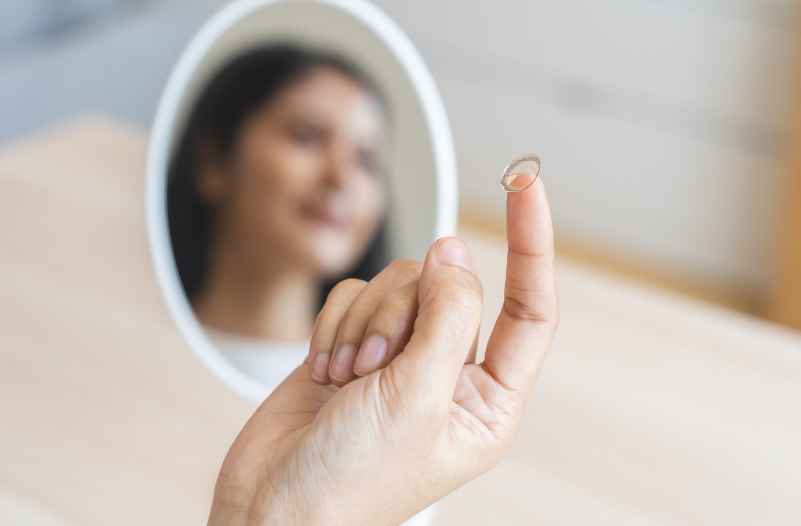 A close up image of a person's hand with a dry-eye compatible contact lens on their index finger.