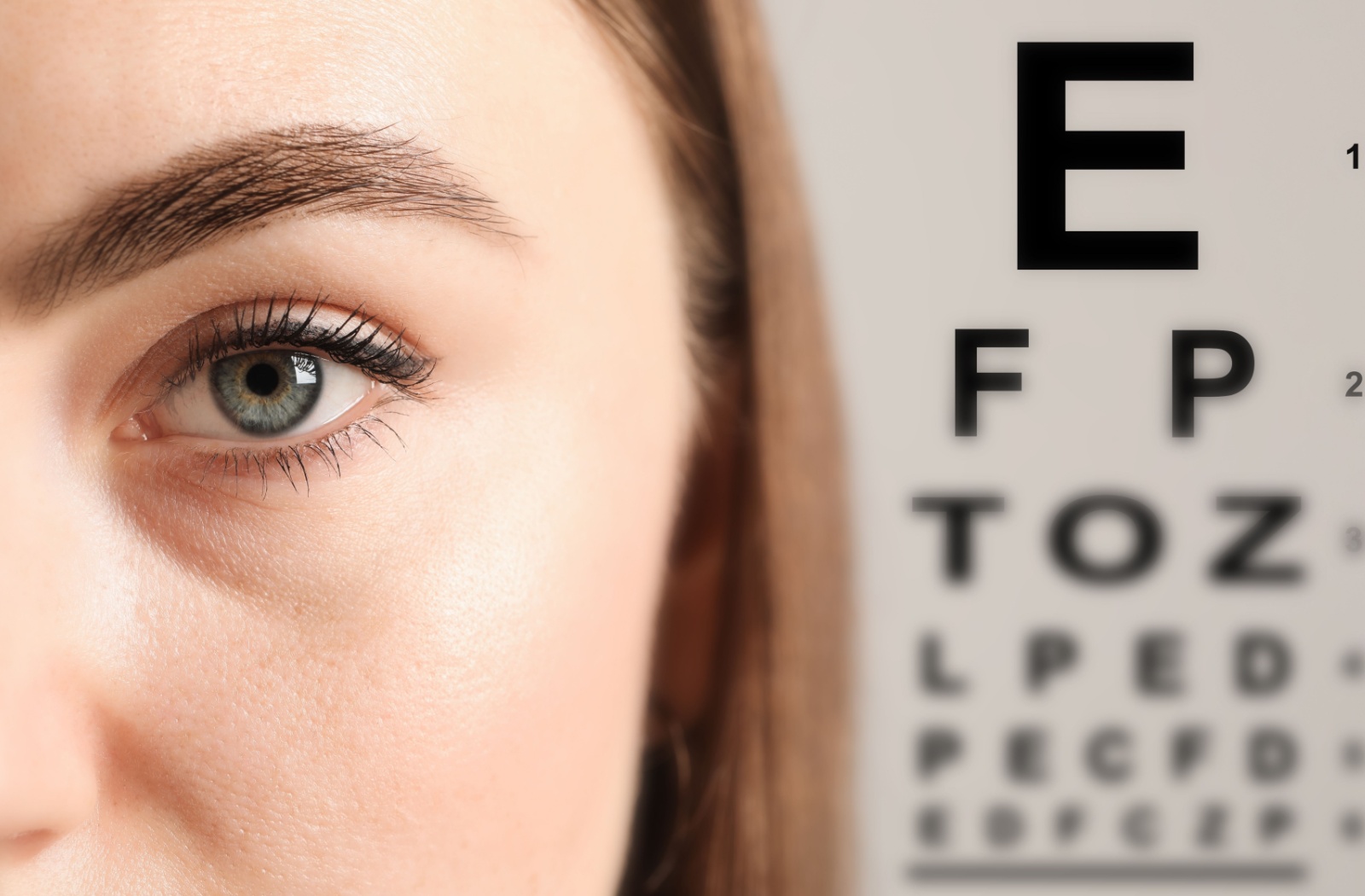 A close-up image of a patient's face during an eye exam with a letter chart in the background.