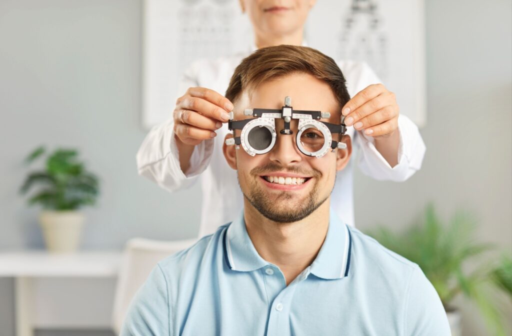A happy, smiling patient during an eye exam while an optometrist fits a phoropter to their face.