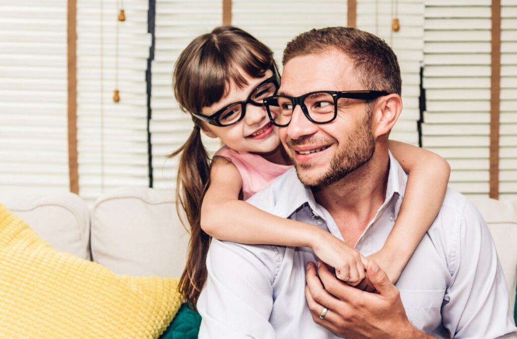 A child wraps their arms around their parent; both are wearing glasses and smiling