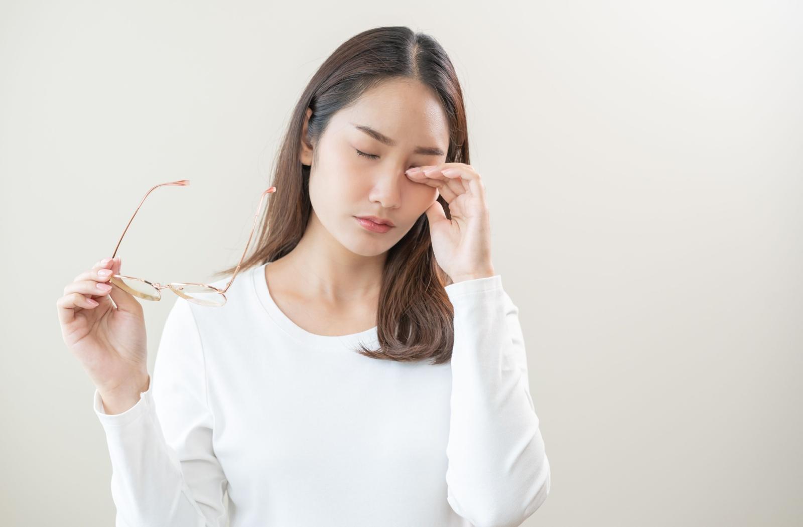 A person holding their glasses in one hand and rubbing their irritated eye with the other